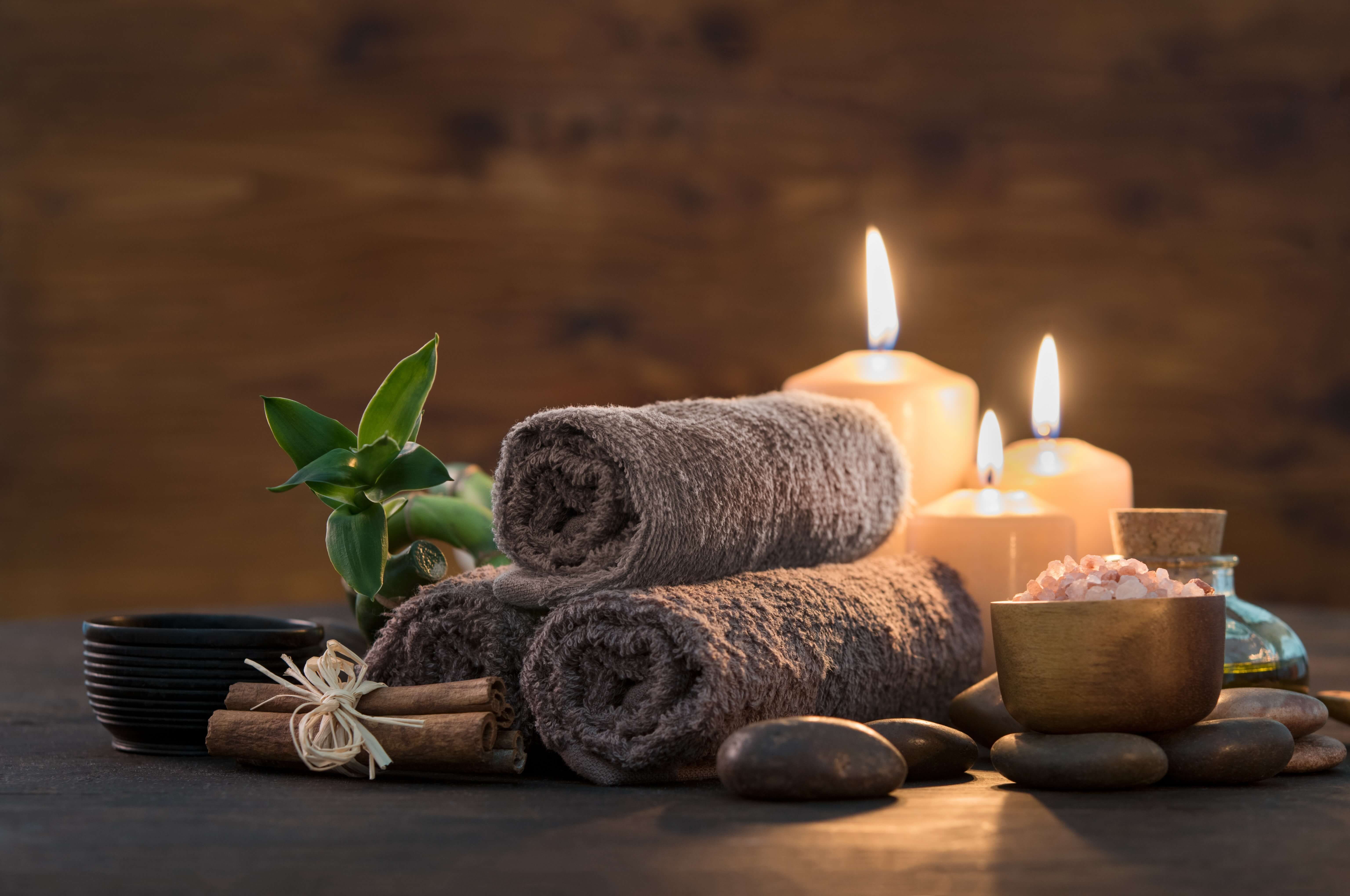 Lit candles, rolled towels and massage stones on a dark wooden table